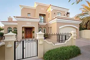 Large house with a fence and a garage in front. The house has multiple stories, a balcony, and palm trees in the background.